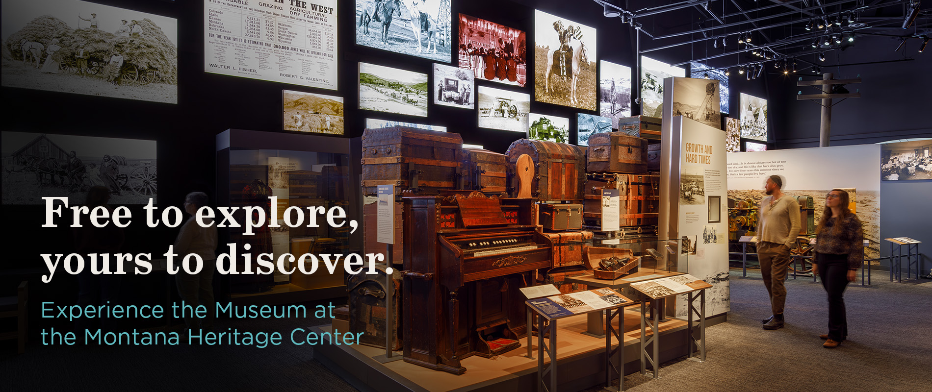 A display within the Montana Homeland gallery featuring historical trunks, a piano and a wall full of historical photos