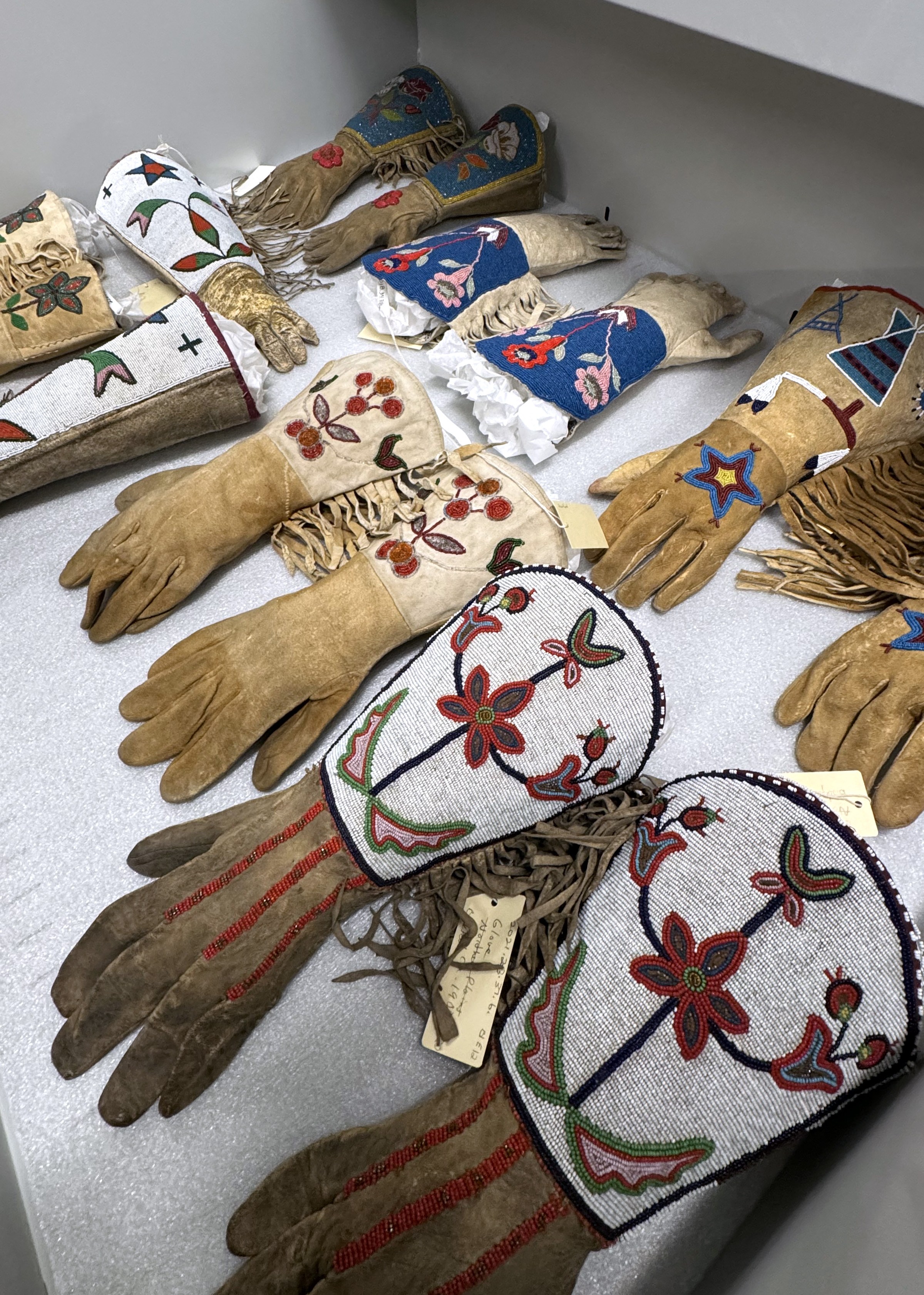 A drawer filled with beaded gloves with intricate patterns